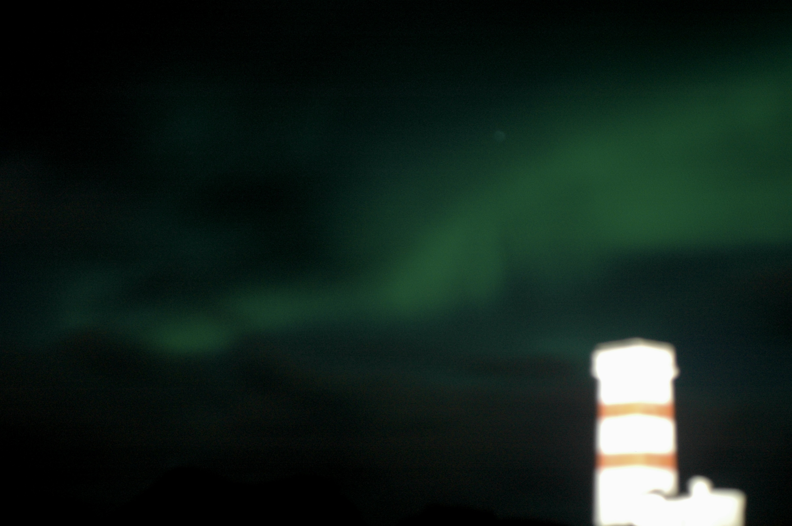 Out of focus photo of the norther lights in Iceland. There is an out of focus lighthouse in the foreground